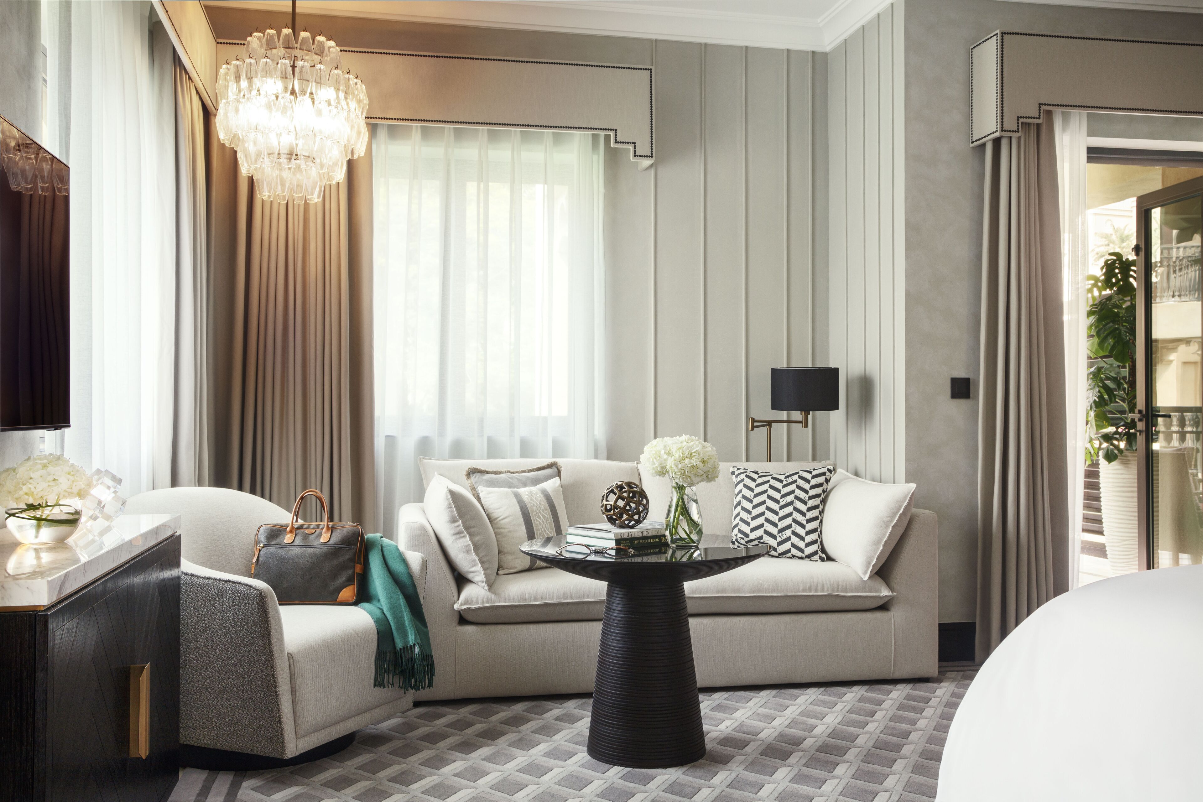 Une chambre d’hôtel moderne avec un canapé, une table ronde, un lustre et une vue sur l’extérieur.