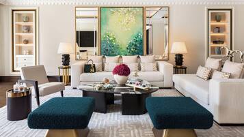 Un salon moderne comprenant un canapé, deux poufs, une table basse et des objets décoratifs. On y trouve deux lampes, un vase avec des fleurs et un tableau accroché au mur.