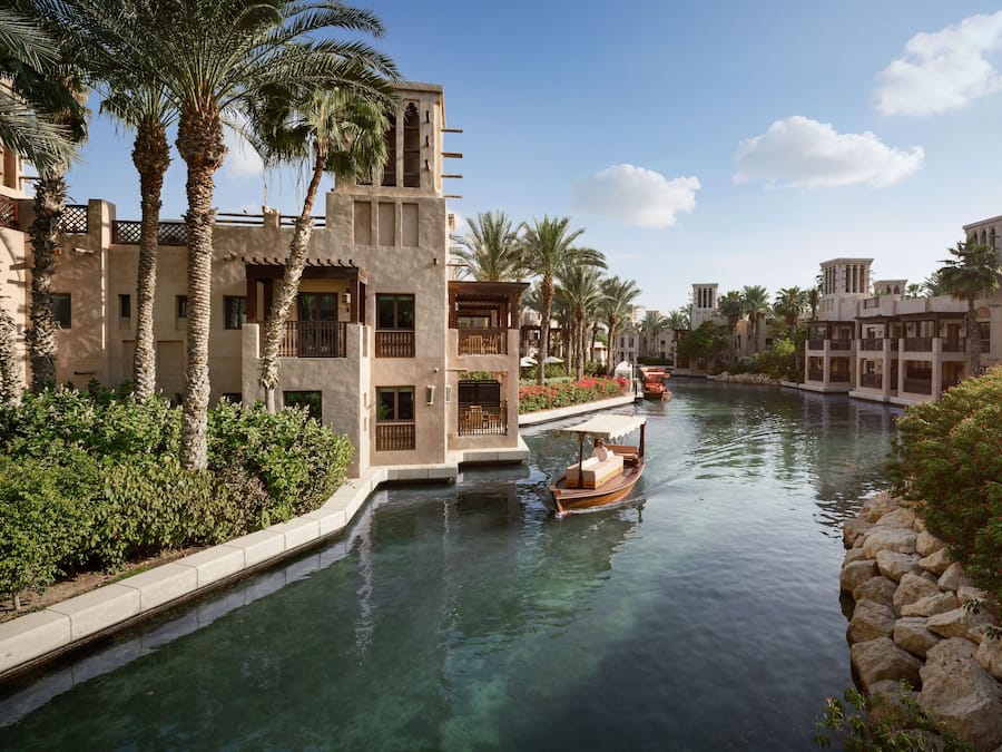 A canal with a boat, palm trees, and buildings with traditional architecture.