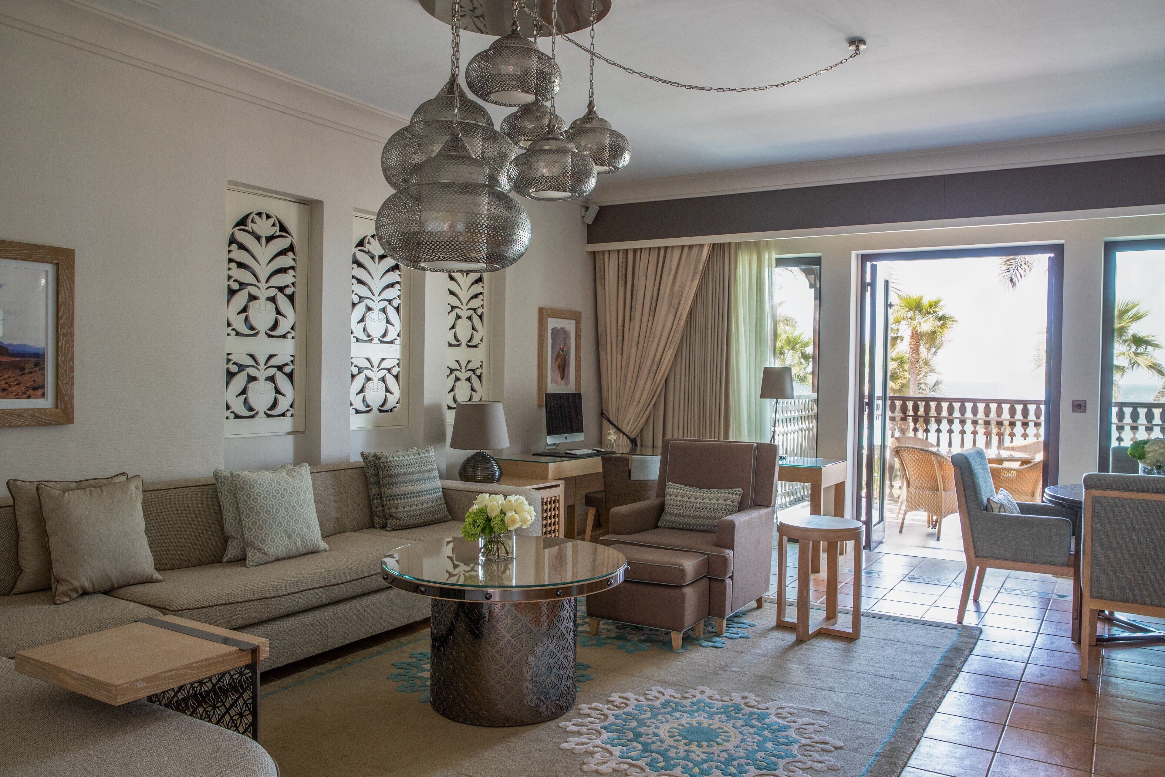 Un salon moderne comprenant un canapé, des fauteuils, une table basse et un balcon aménagé avec du mobilier d’extérieur.