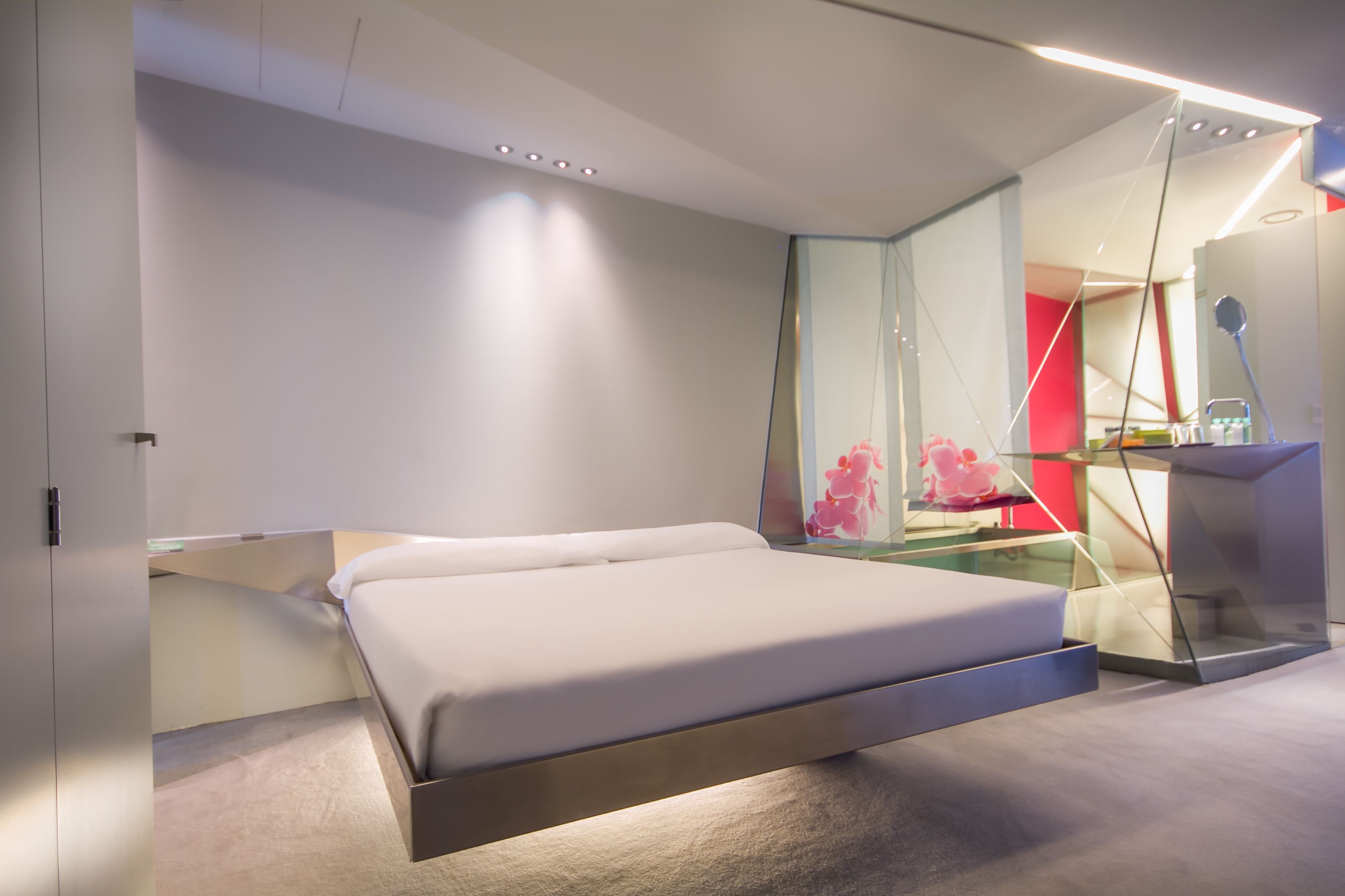 Un dormitorio moderno con una cama, un escritorio de vidrio y una pared de acento roja.