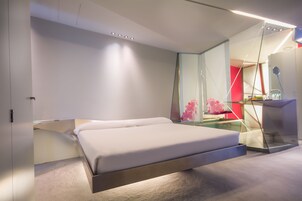 Una camera da letto moderna con un letto, una scrivania in vetro e una parete di colore rosso.