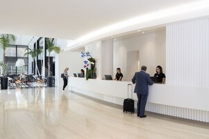 Una moderna area reception con una scrivania bianca, diversi impiegati e un uomo con una valigia.