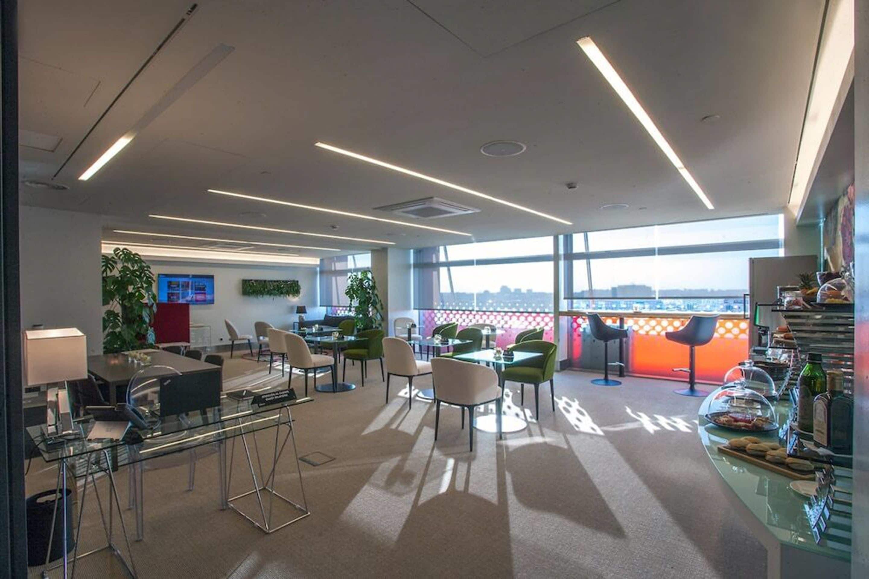Un espacio de oficina moderno con paredes de vidrio, diversas opciones de asientos y vistas de la ciudad a través de amplias ventanas.