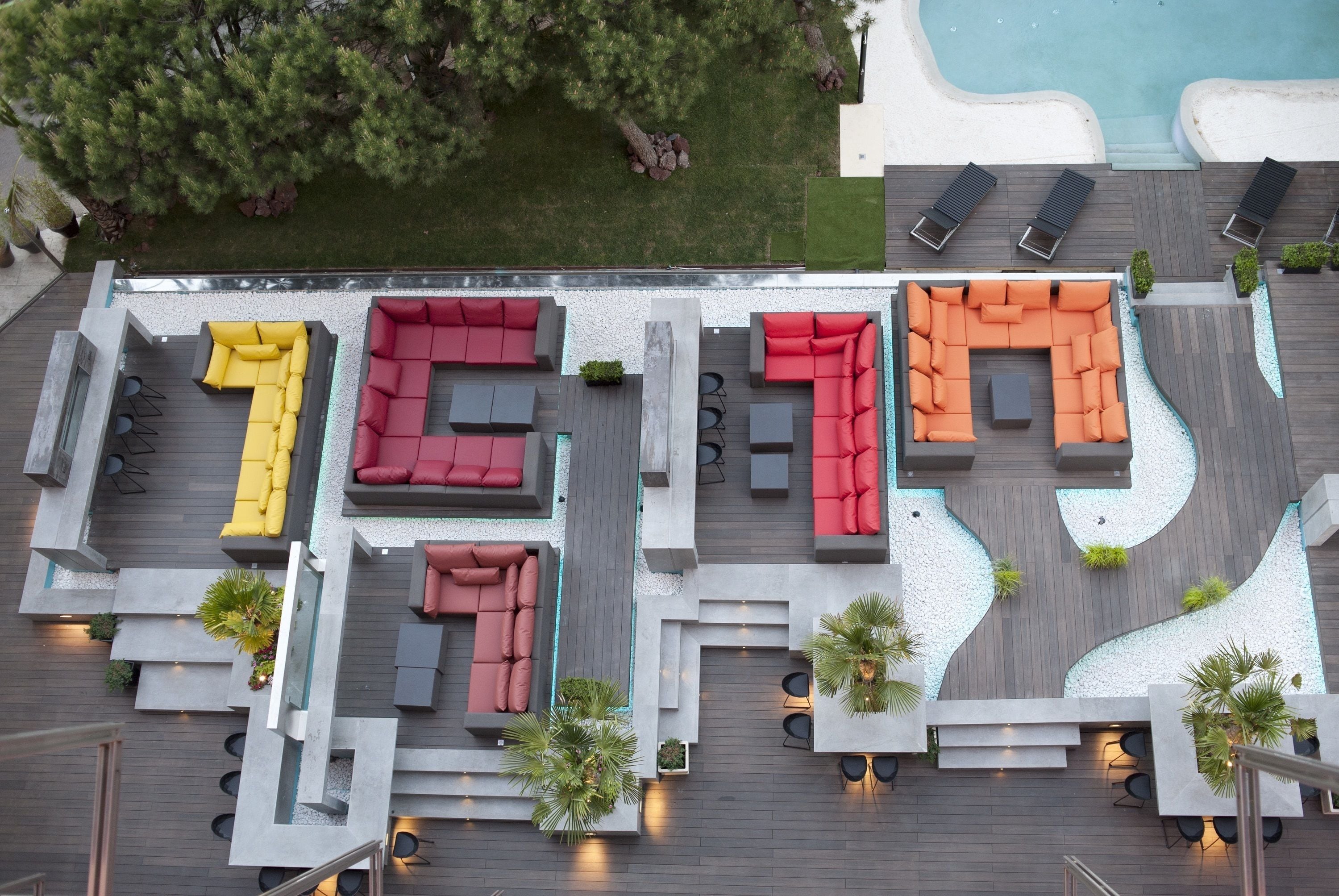 Vista aèria d'una zona de terrat amb diverses zones d'estar, una piscina i vegetació als voltants.