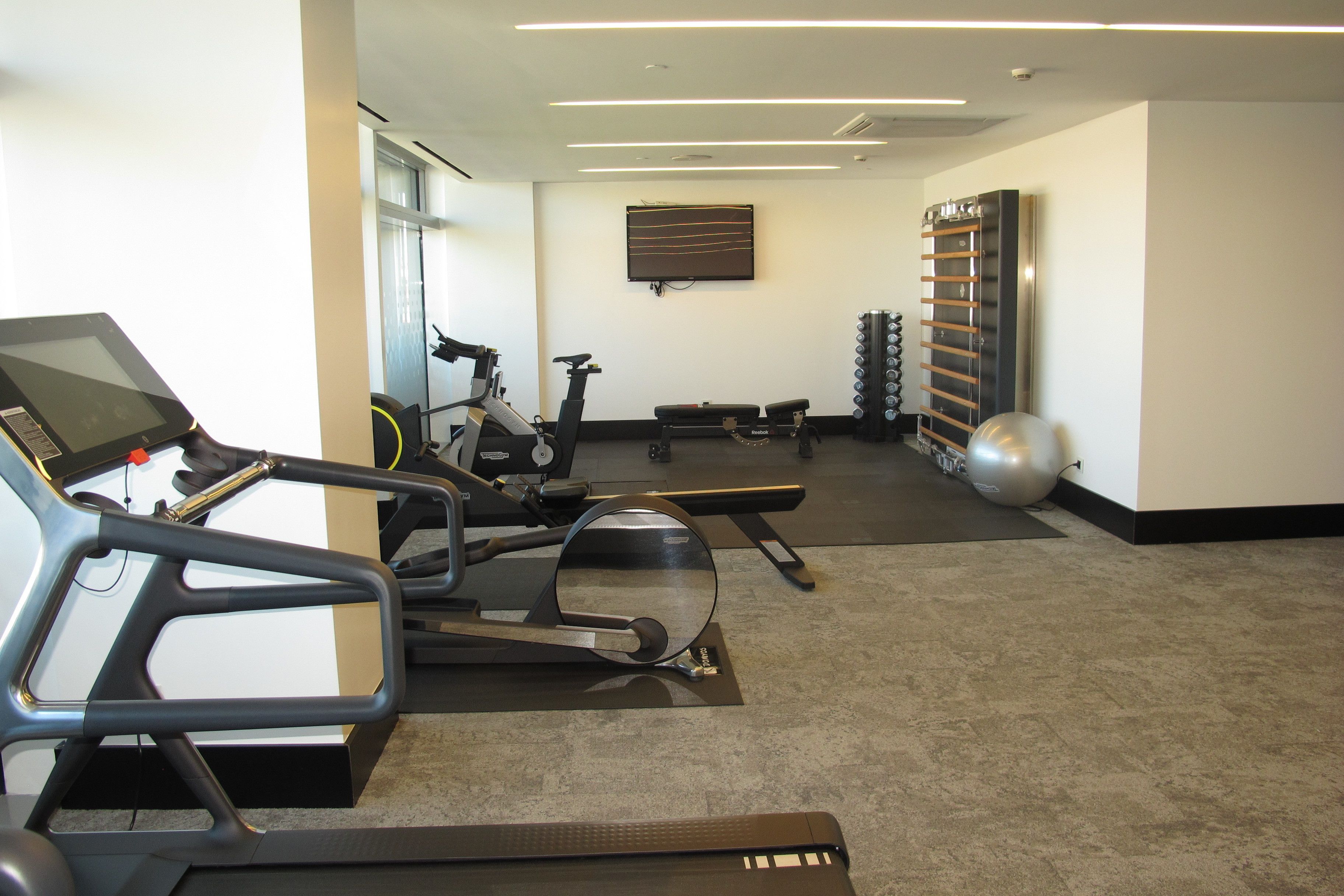 Une salle de sport équipée de matériel d’exercice, notamment des tapis de course, des vélos d’appartement et des poids.