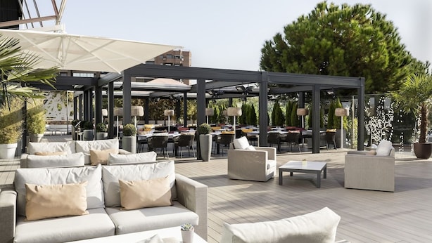 An outdoor seating area with sofas and tables, umbrellas, and potted plants. - Hotel Puerta América (Madrid)
