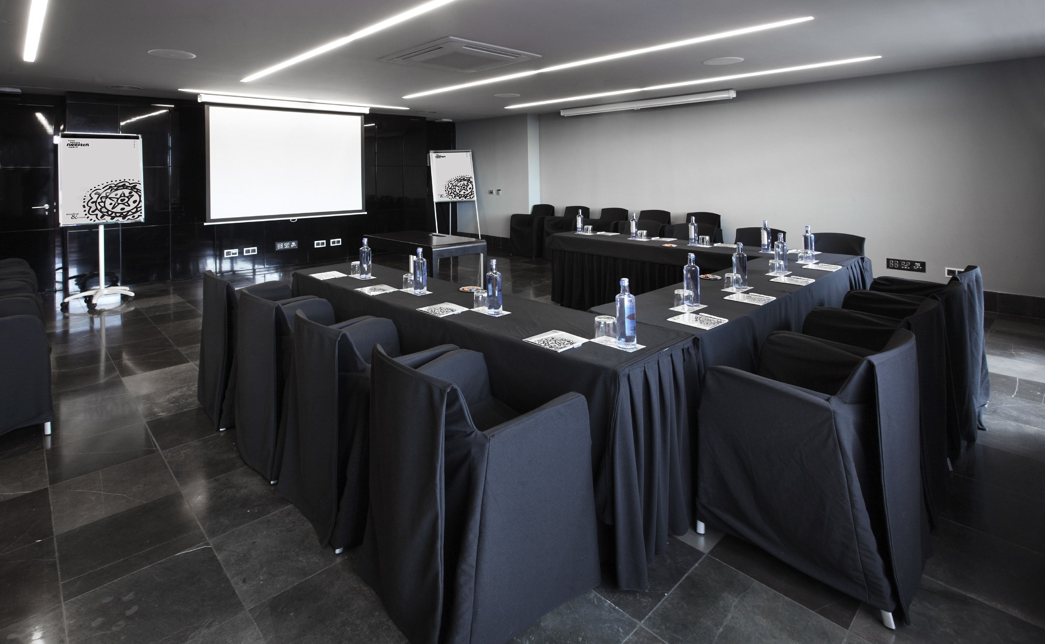 Ein Konferenzraum mit langem Tisch, Stühlen und einer Projektionsleinwand.