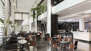 A modern hotel lobby with a mix of seating areas, a reception desk, and a bar. - Hotel Puerta América (Madrid)