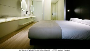 A modern hotel room with a large bed, a vanity with two mirrors, and a dark accent wall. - Hotel Puerta América (Madrid)