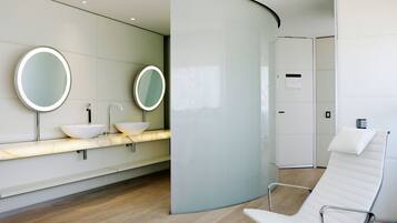 Un baño moderno con dos lavamanos, un espejo y una silla blanca.