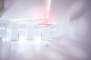 Ein modernes, minimalistisches Zimmer mit weißer Farbgestaltung, das eine außergewöhnliche, gebogene Leuchte und ein schlankes, zeitgemäßes Design aufweist.