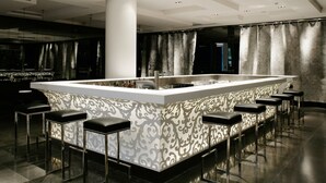 A modern bar area with a central island, bar stools, and patterned wall designs. - Hotel Puerta América (Madrid)