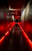 A corridor with red lighting, a ceiling with recessed lights, and a dark floor.