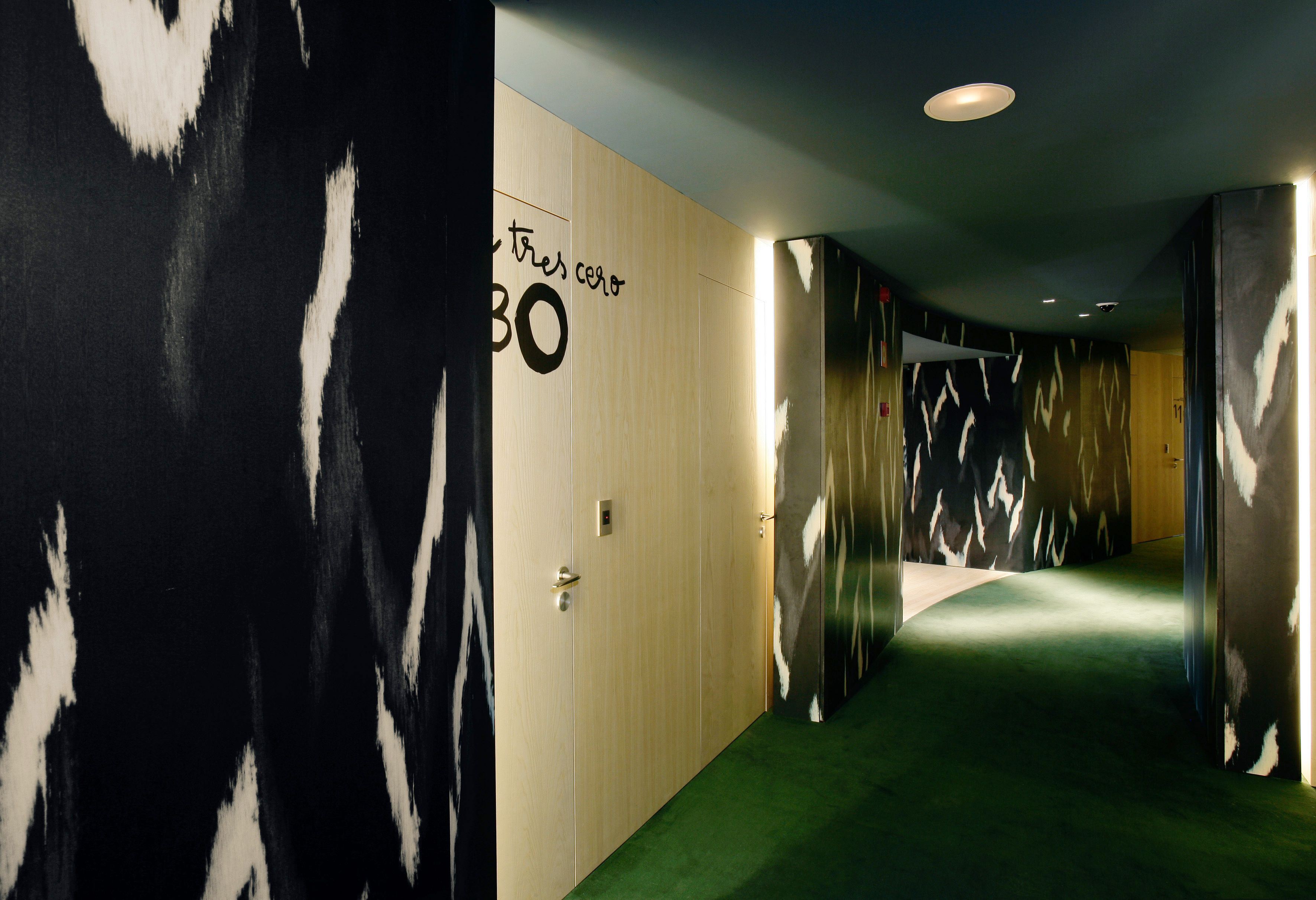 Un corridoio con tappeto verde, pareti in legno e una porta con la scritta 'Tres Color 30'.