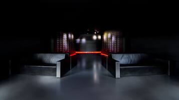 Una habitación oscura con dos sofás de cuero negro orientados hacia una pared con texto iluminado.