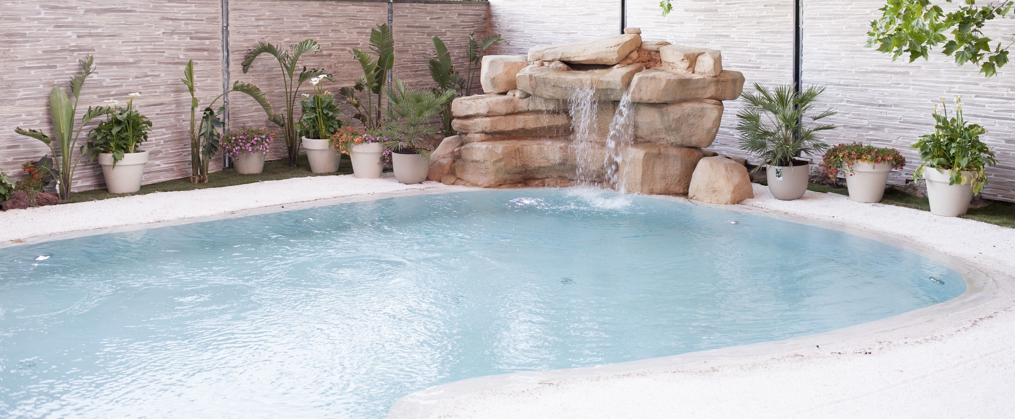 Une piscine agrémentée d’une cascade et entourée de plantes en pot.