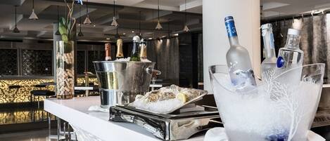 A bar area with a white countertop, ice buckets, bottles, and a tray of oysters.