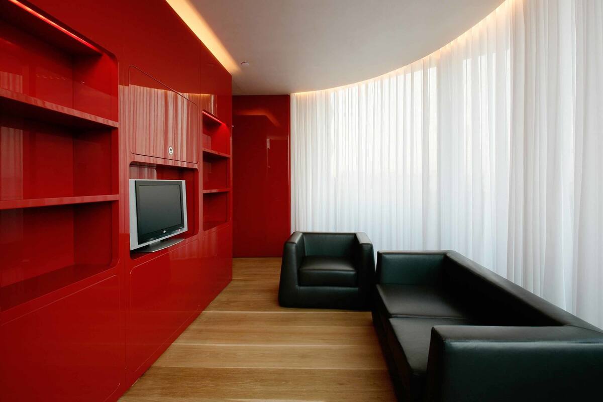 A modern living room with red walls, a flat-screen TV, and black leather sofas.
