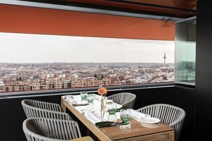 Un comedor con una mesa dispuesta para dos, con vistas a un paisaje urbano donde destaca una torre.