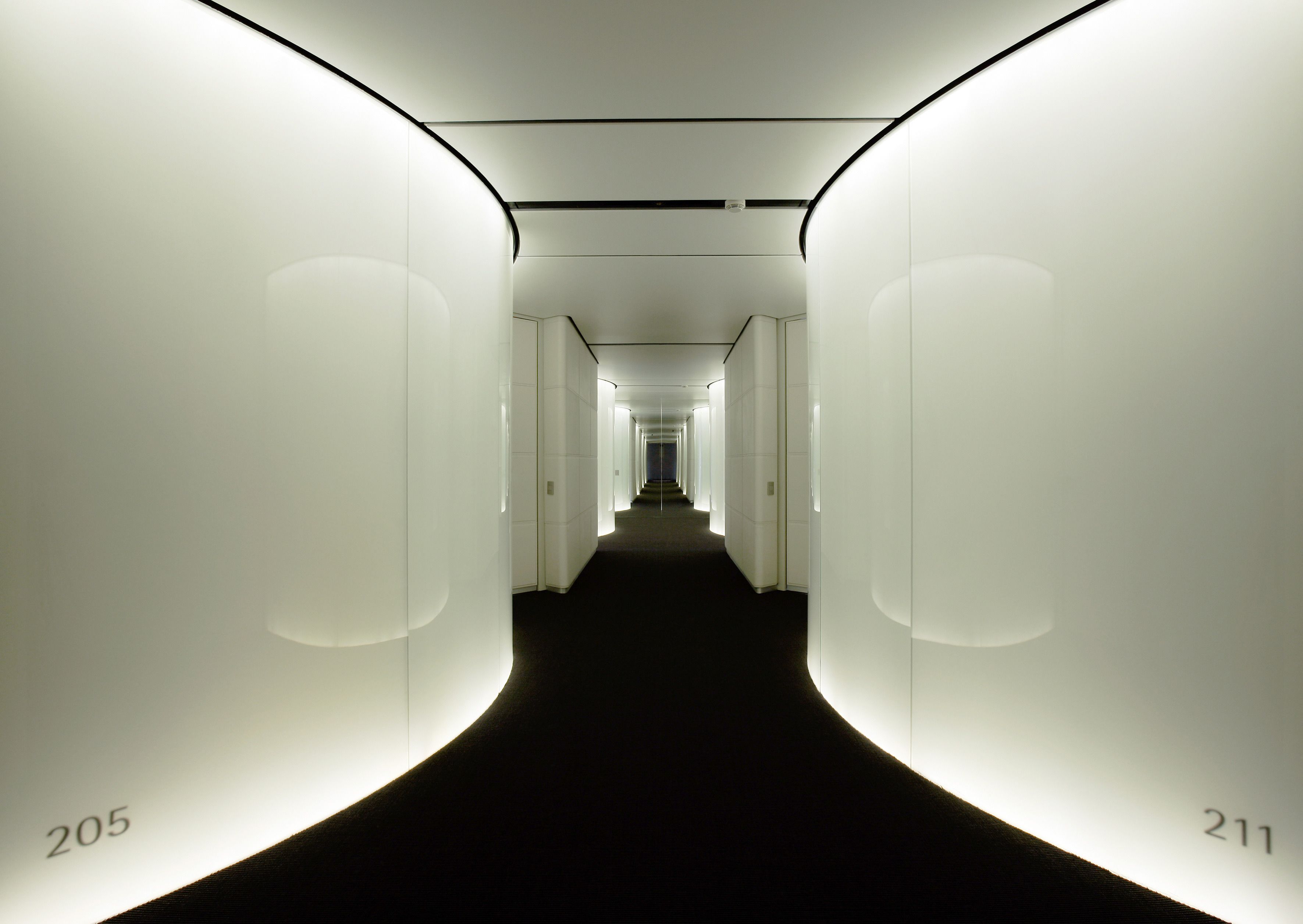A hallway with white walls and a black carpet, numbers 205 and 211 visible.