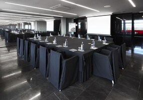 Ein Konferenzraum mit einem langen Tisch, Stühlen und einer Projektionsleinwand.