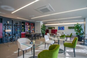 A modern office space with glass tables, green chairs, and a variety of shelves with items.
