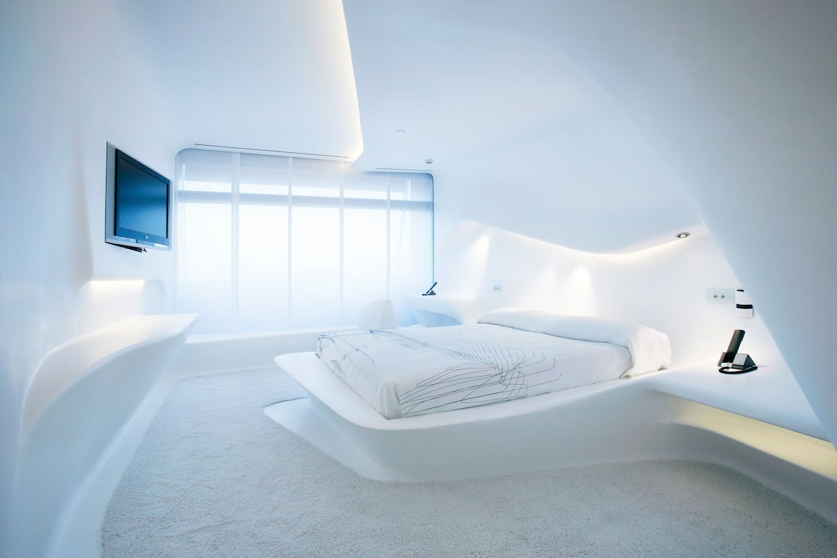A modern bedroom with a curved bed, a flat-screen TV, and a large window.