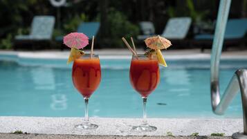 Two cocktails with umbrellas by a poolside, with lounge chairs and a pool in the background.