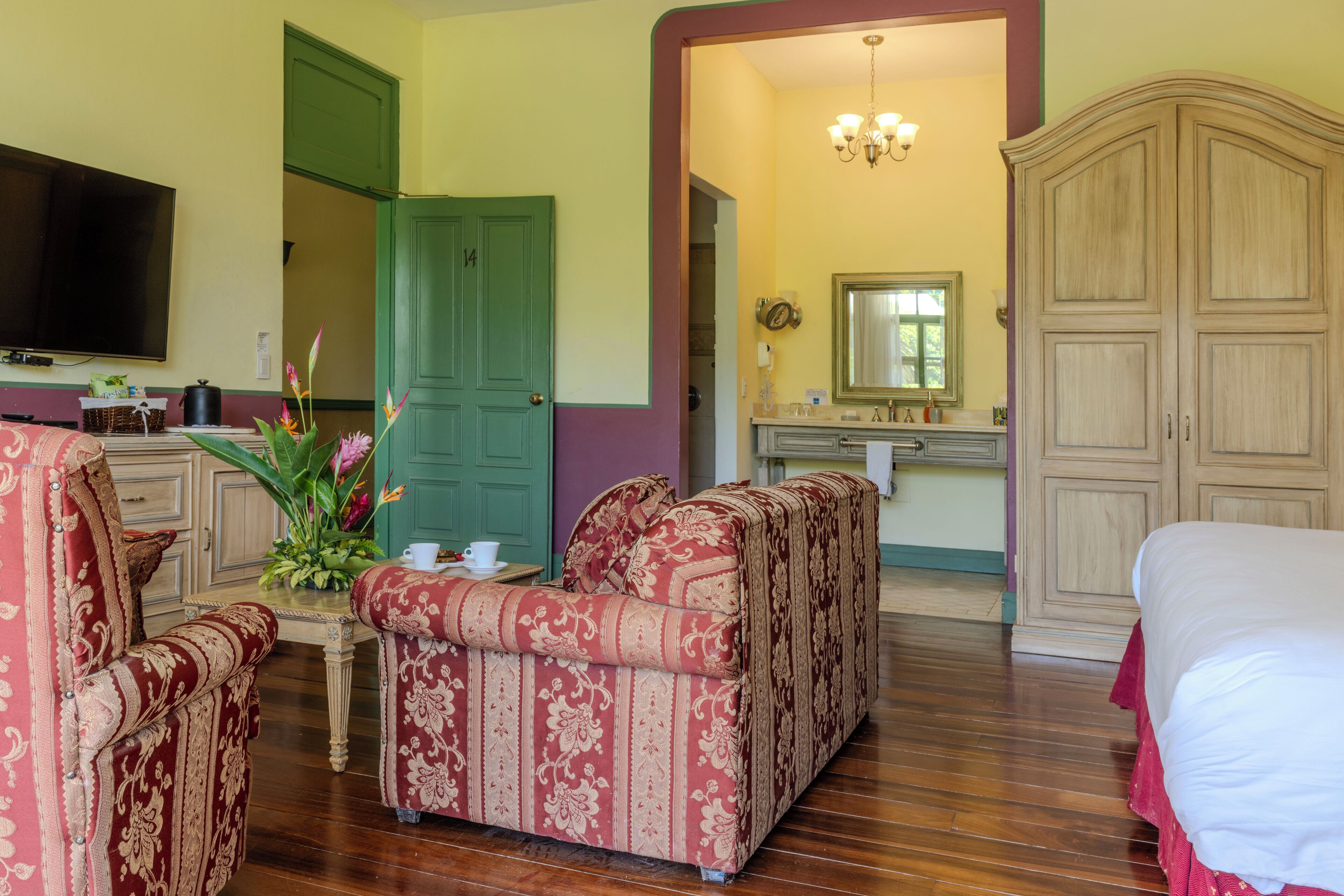 Habitación de hotel con sofá, televisor, mesa de comedor con un florero y un amplio armario.