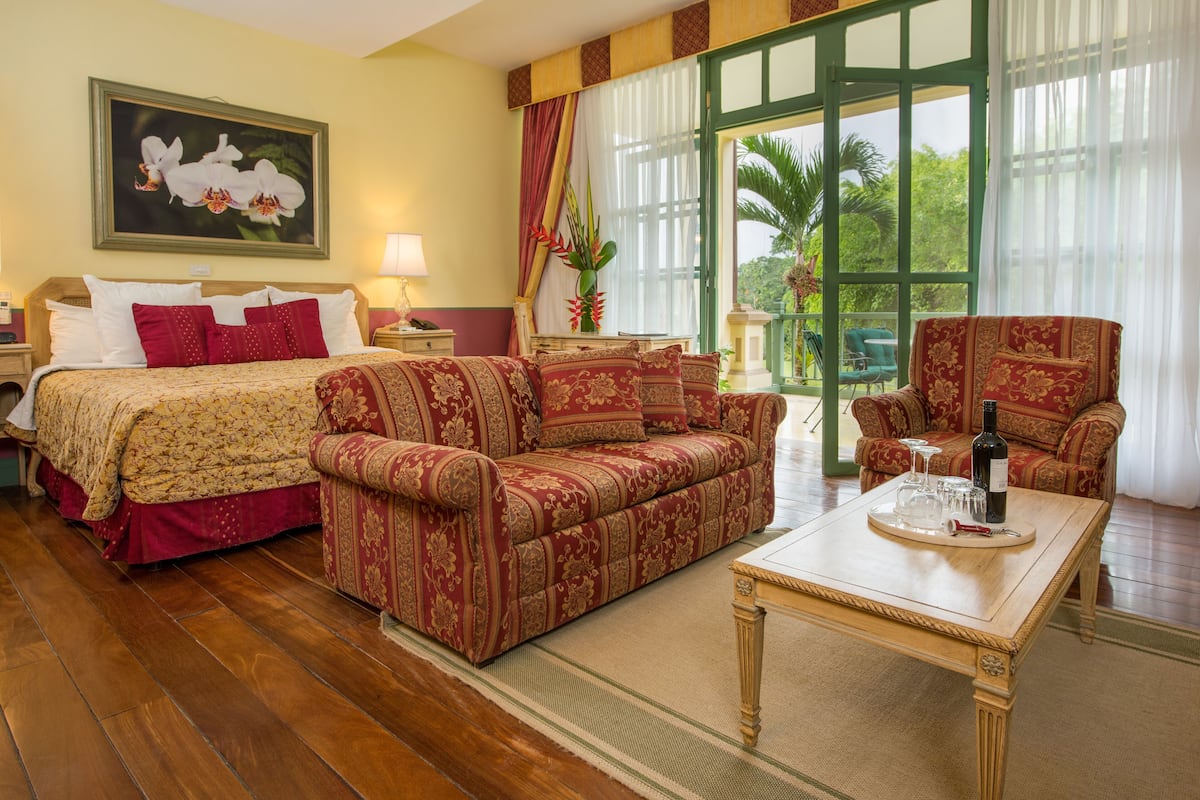A hotel room with a bed, two sofas, a coffee table, and a view of greenery outside.