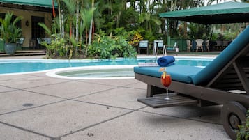 A poolside lounge area with a sunbed, a pool, and surrounding greenery.