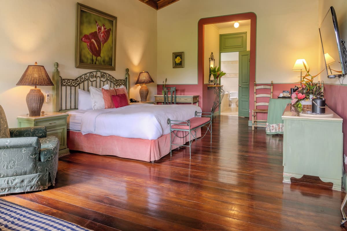 A bedroom with a large bed, two bedside tables with lamps, a chair, a desk, and a mirror.