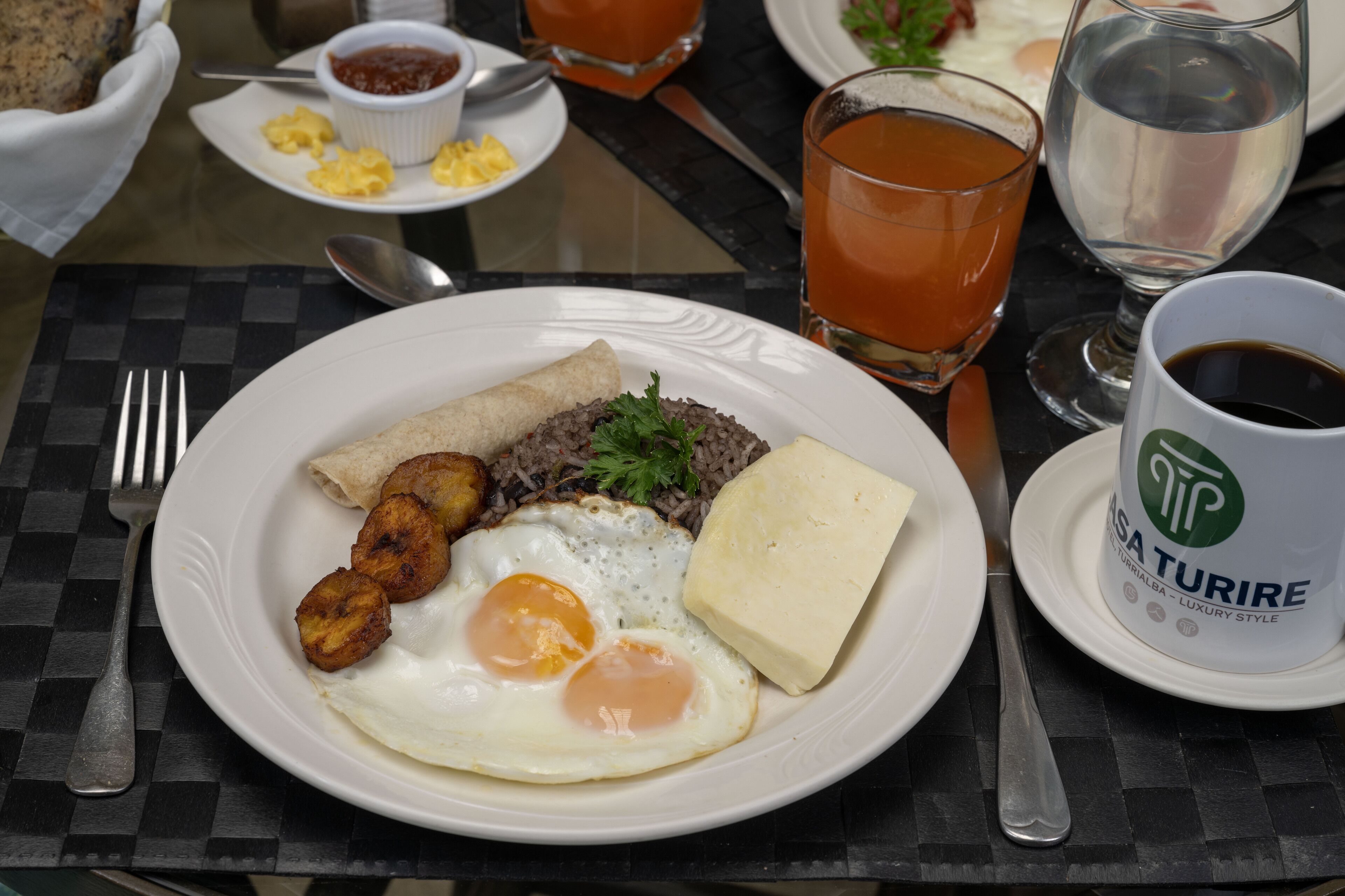 A breakfast plate with eggs, plantains, and a piece of cheese on a checkered tablecloth.