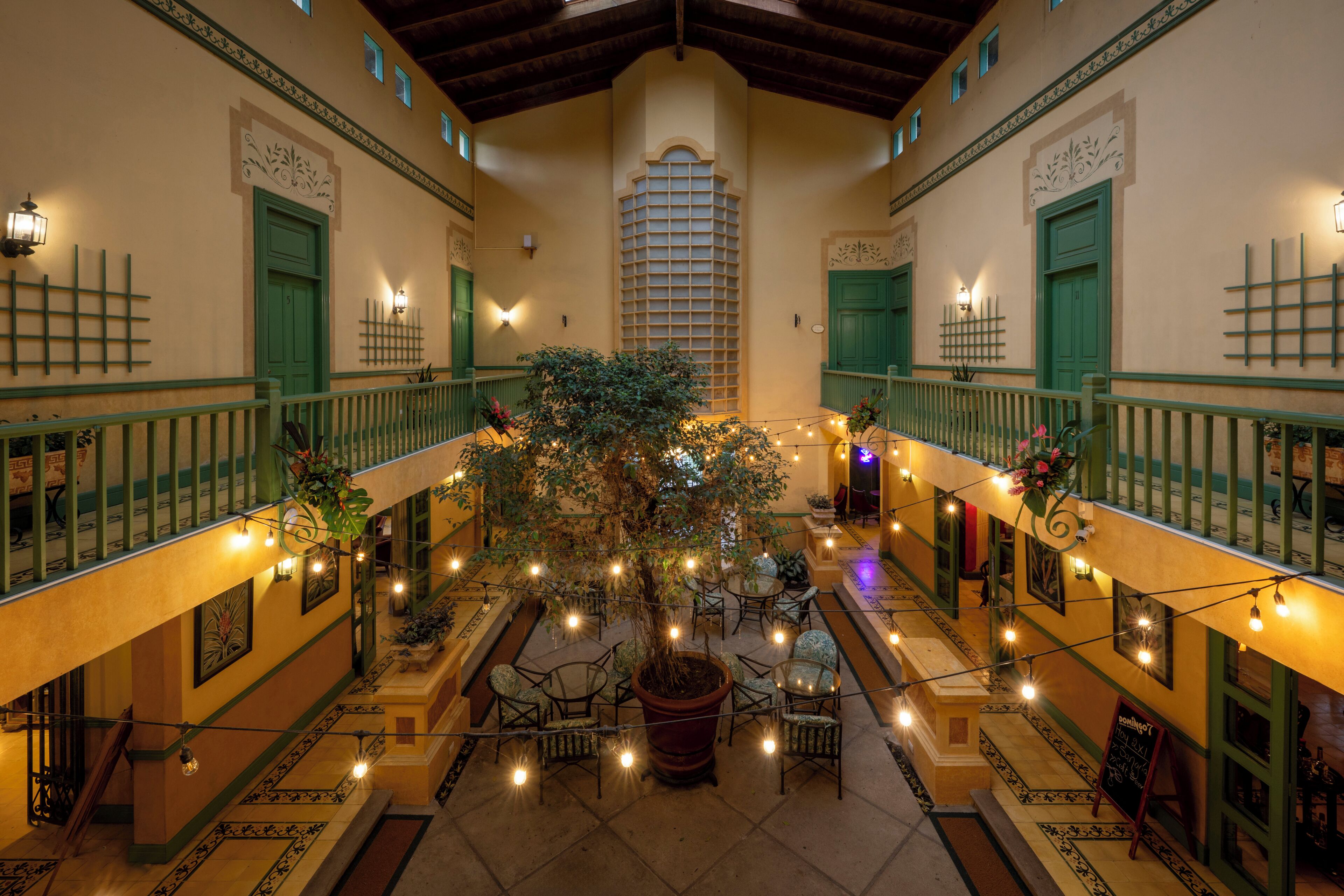 Un patio central con un árbol, rodeado de asientos y luces colgantes.