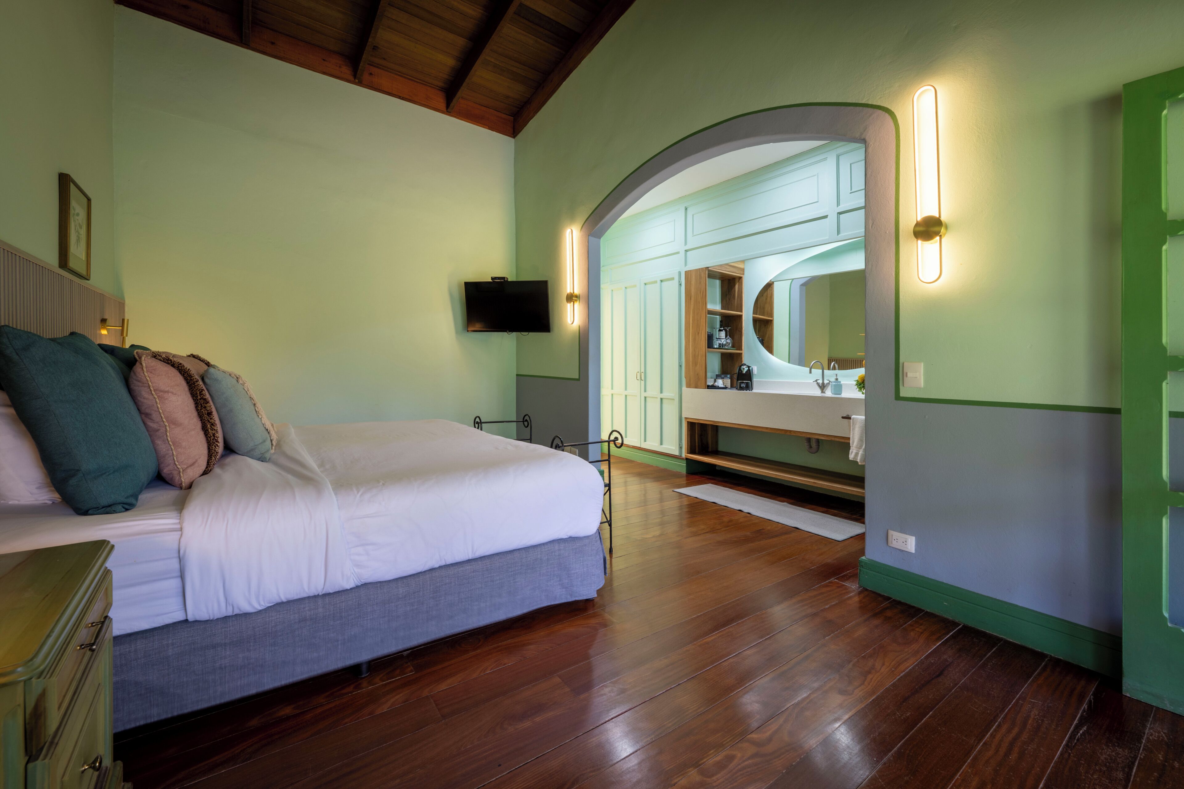 A bedroom with a bed, a television, a mirror, and a wooden floor.