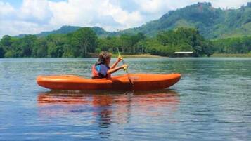 Une personne dans un kayak orange sur un lac calme, avec une colline boisée en arrière-plan.