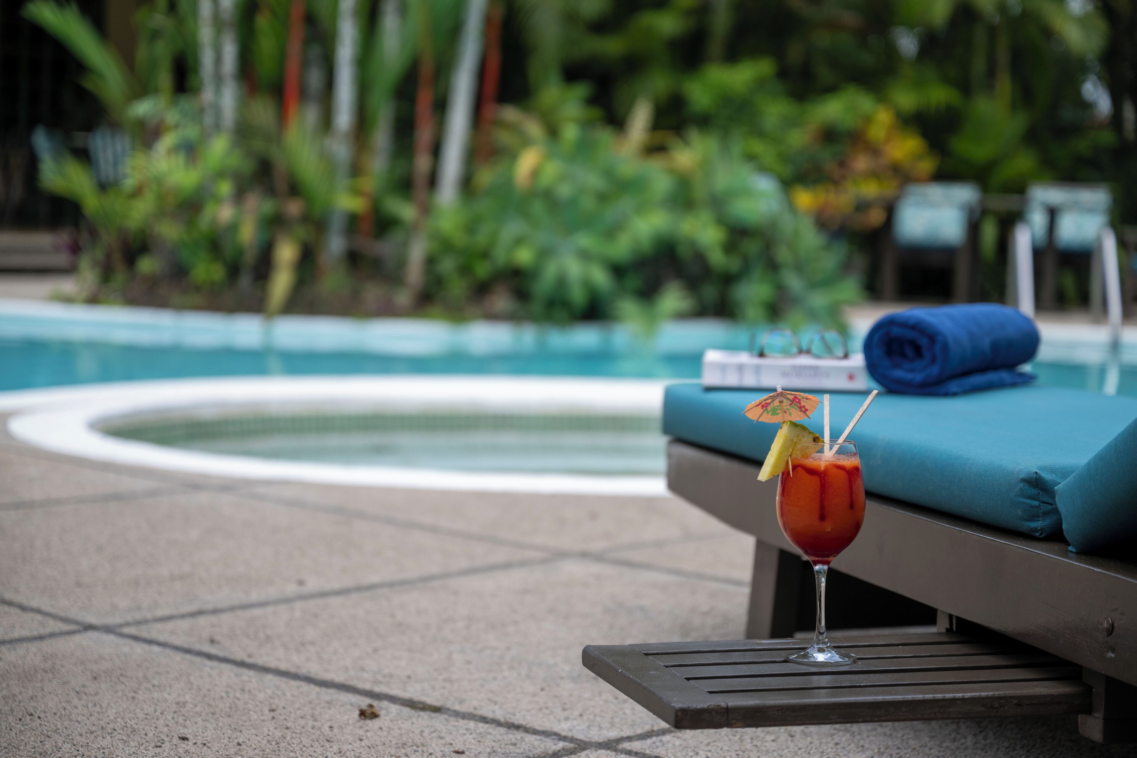 Área ao lado da piscina com uma espreguiçadeira e uma bebida sobre a mesa.
