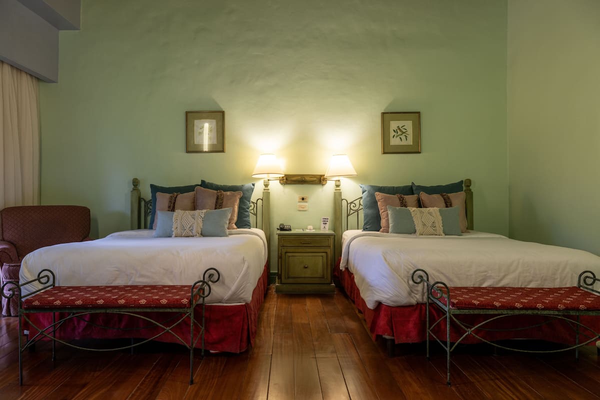 A hotel room with two beds, a nightstand, and a chair.