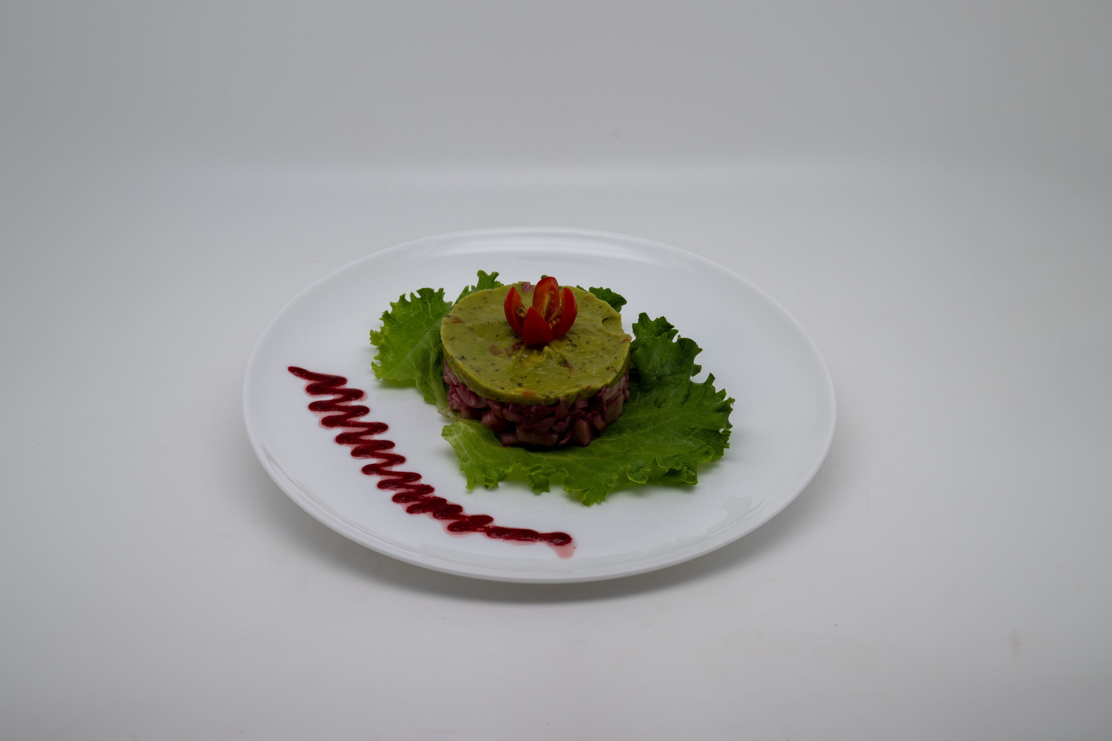 A white plate with a layered food item, garnished with a cherry and surrounded by green lettuce leaves.