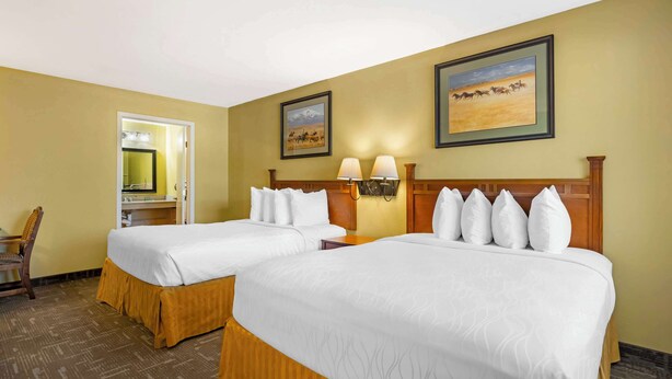A hotel room with two beds, a wooden headboard, a nightstand, and a mirror. - Best Western Executive Inn (Hallettsville)