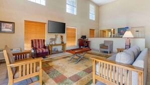 A spacious living room with a large sofa, wooden chairs, a coffee table, and a flat-screen TV mounted on the wall. - Best Western Executive Inn (Hallettsville)
