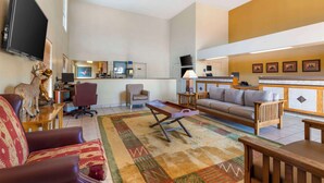 A spacious living room with a sofa, a coffee table, and a television mounted on the wall. - Best Western Executive Inn (Hallettsville)