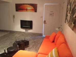 A living room with a flat-screen TV, a sofa, a coffee table, and a door with a sign.
