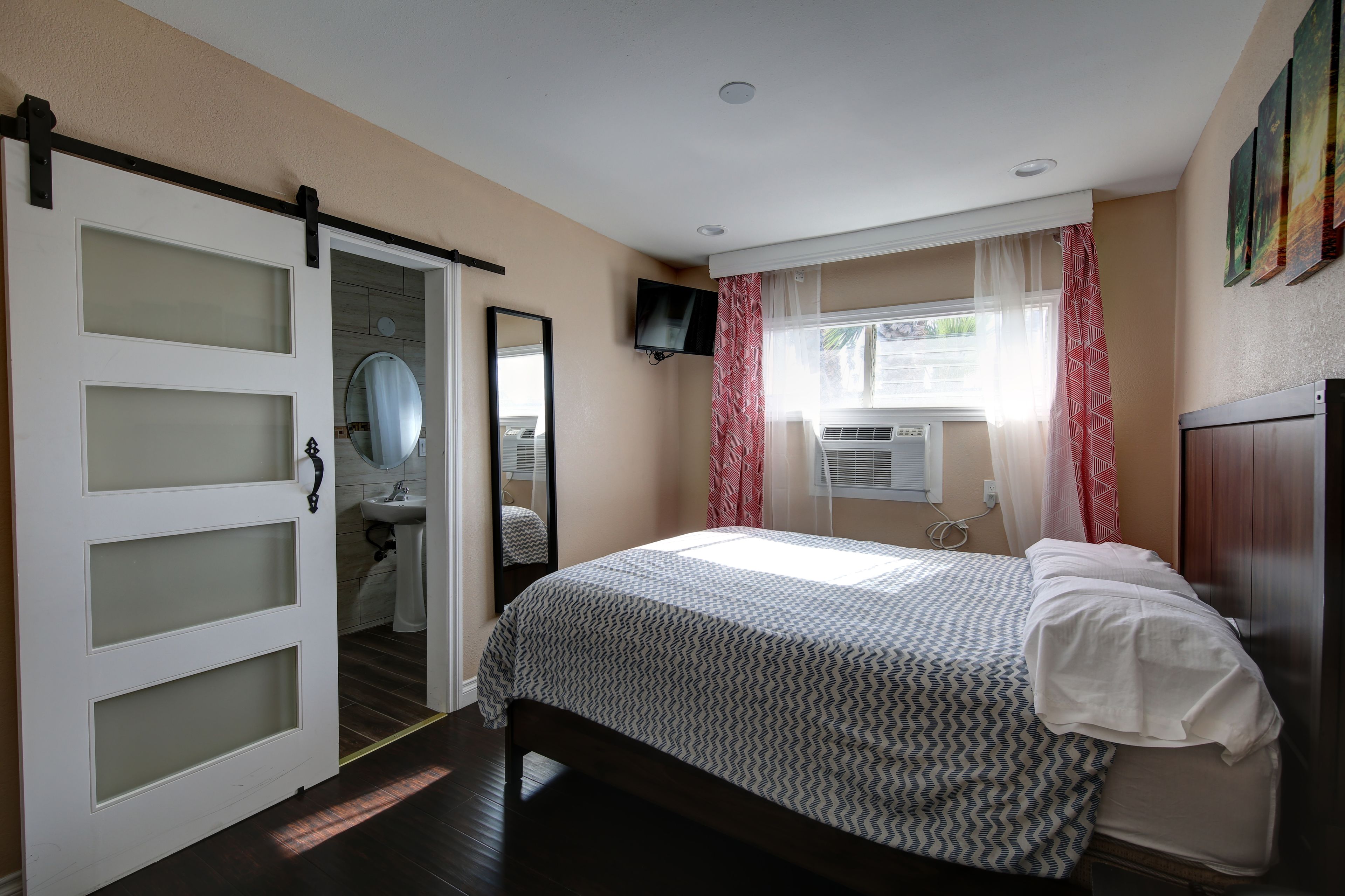 A bedroom with a bed, a bathroom with a sink, a mirror, and a TV mounted on the wall.