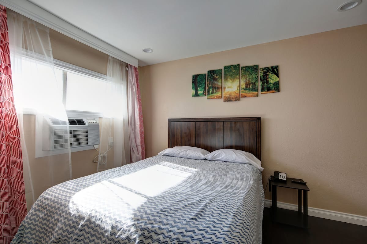 Una habitación de hotel con una cama, una mesita de noche con teléfono y una ventana con cortinas.
