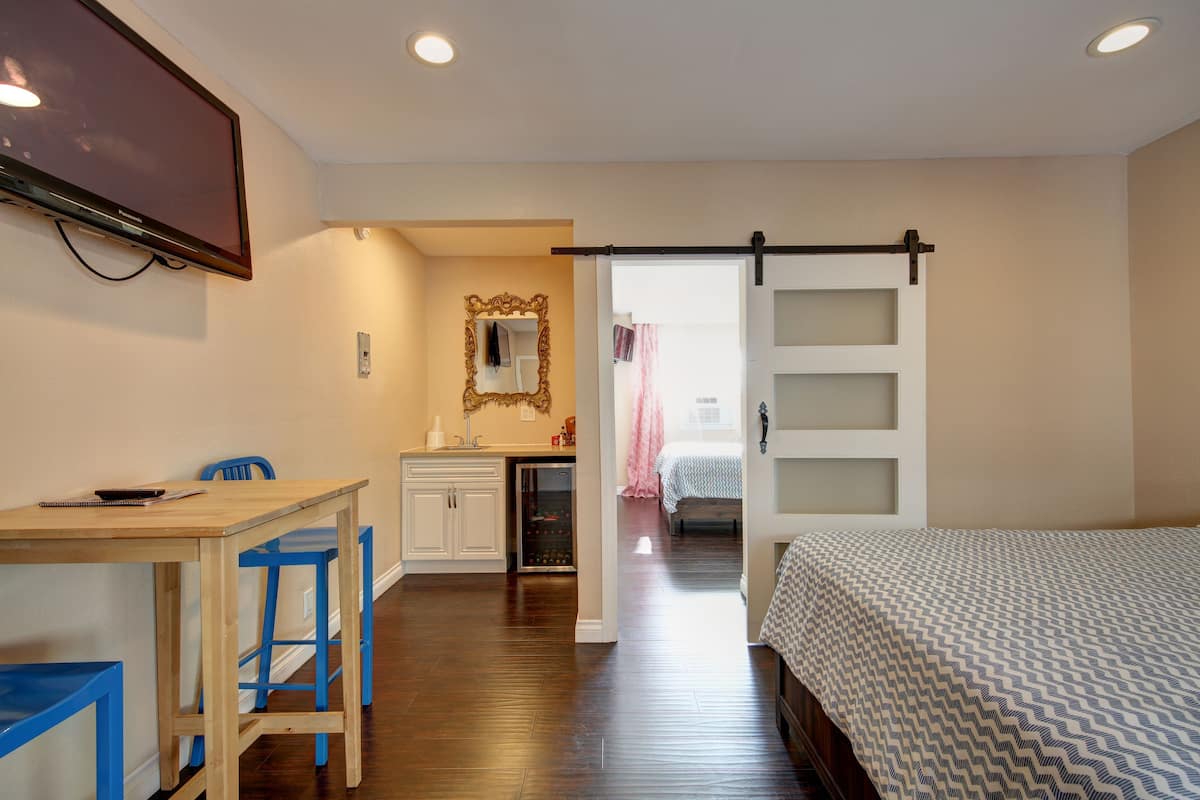 Un dormitorio con una cama, un escritorio con sillas, un espejo y una puerta corrediza que da a otra habitación.