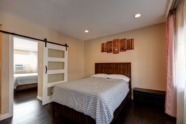 A bedroom with a bed, a bench, a sliding door, and a wall with artwork.