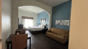 A hotel room with a bed, a sofa, a desk with a chair, and artwork on the wall.