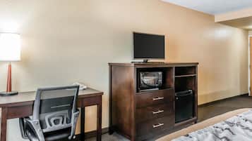 A hotel room with a desk, a chair, a television on a cabinet, a microwave, and a bed.